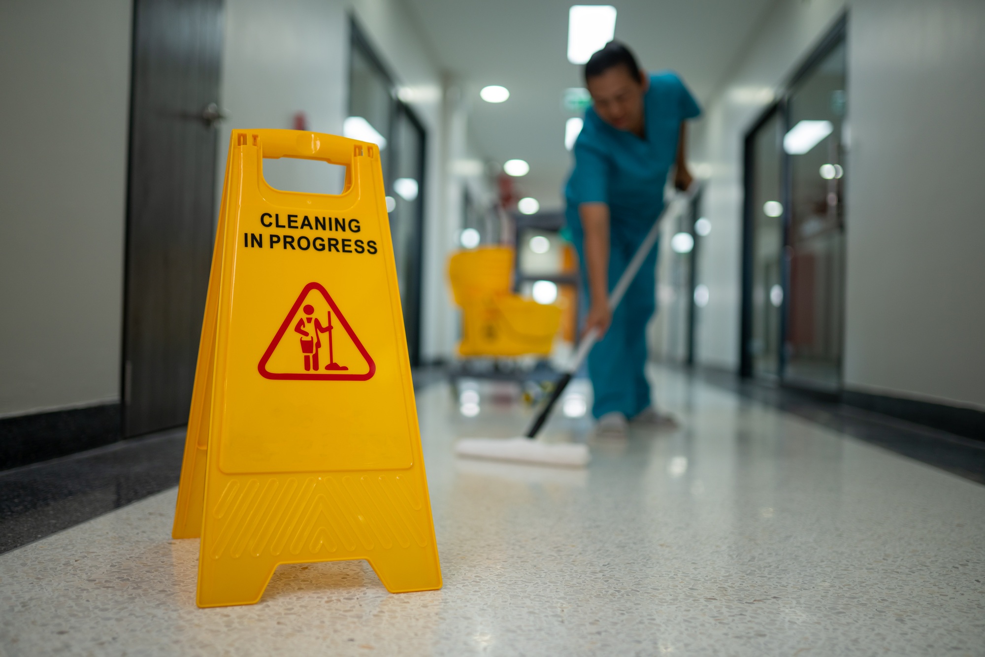 A woman is cleaning a floor with a yellow sign that says "cleaning in progress"