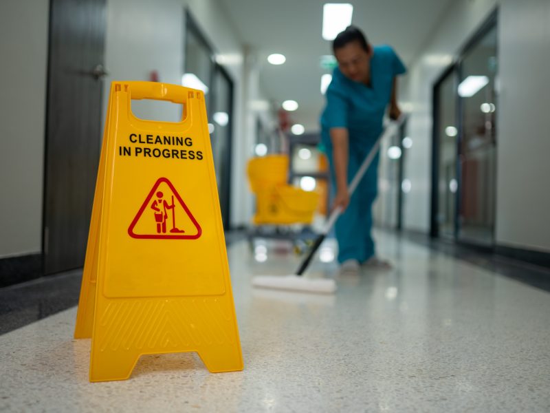 A woman is cleaning a floor with a yellow sign that says "cleaning in progress"