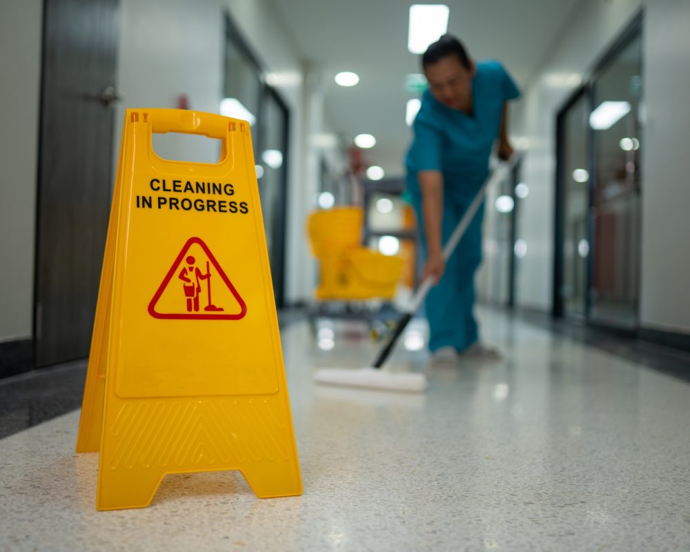 A woman is cleaning a floor with a yellow sign that says "cleaning in progress"