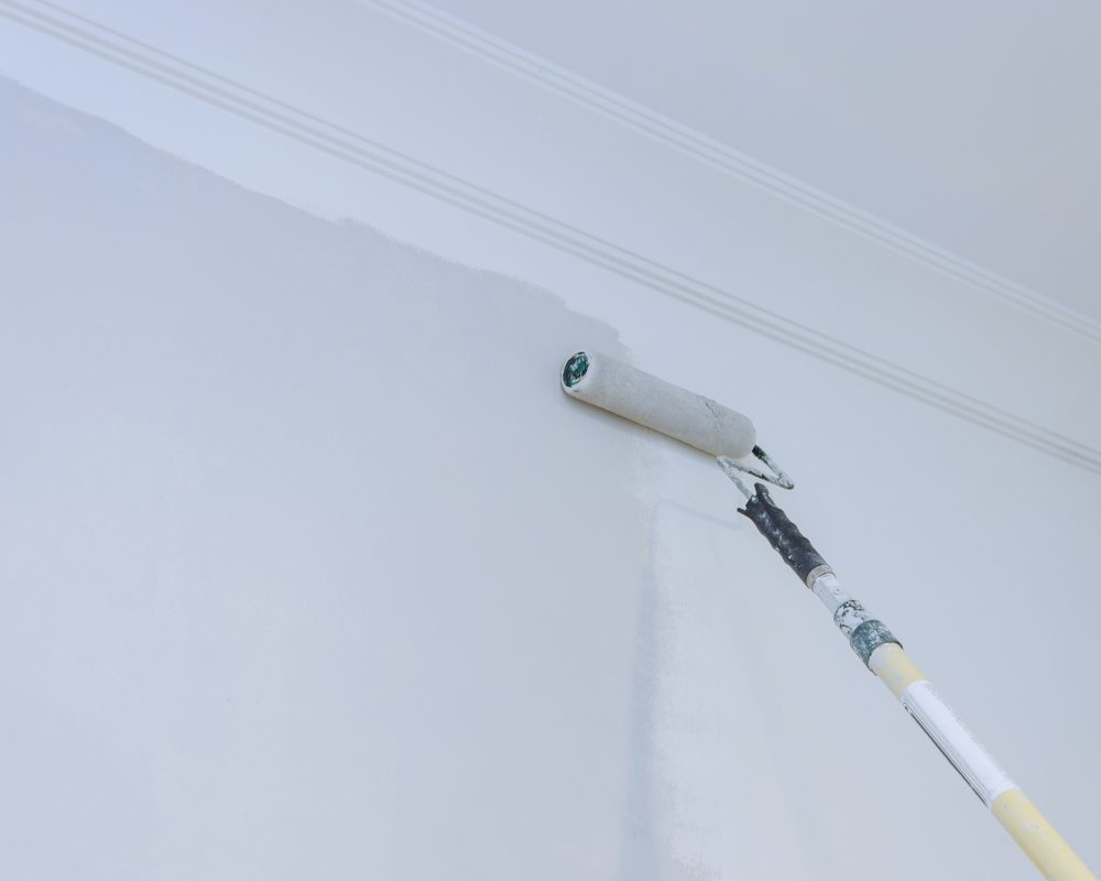 View of painter man painting the wall, with paint roller on empty space